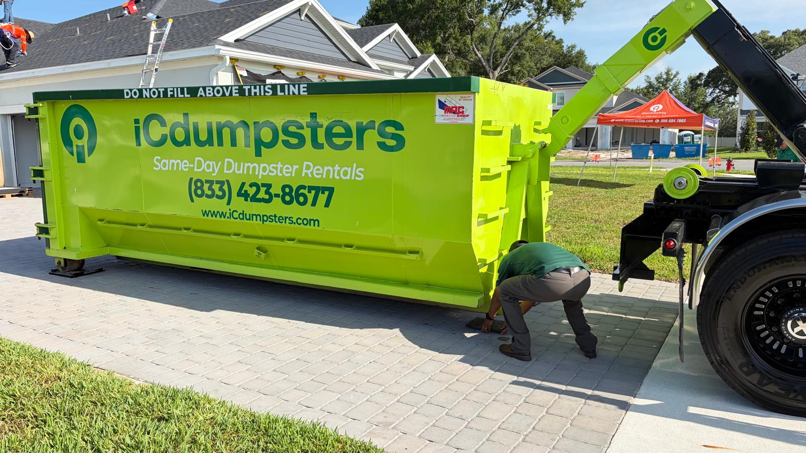 Green iCdumpsters roll-off container sitting on Rolliskate underlayment showing driveway protection during a roofing tear-off job